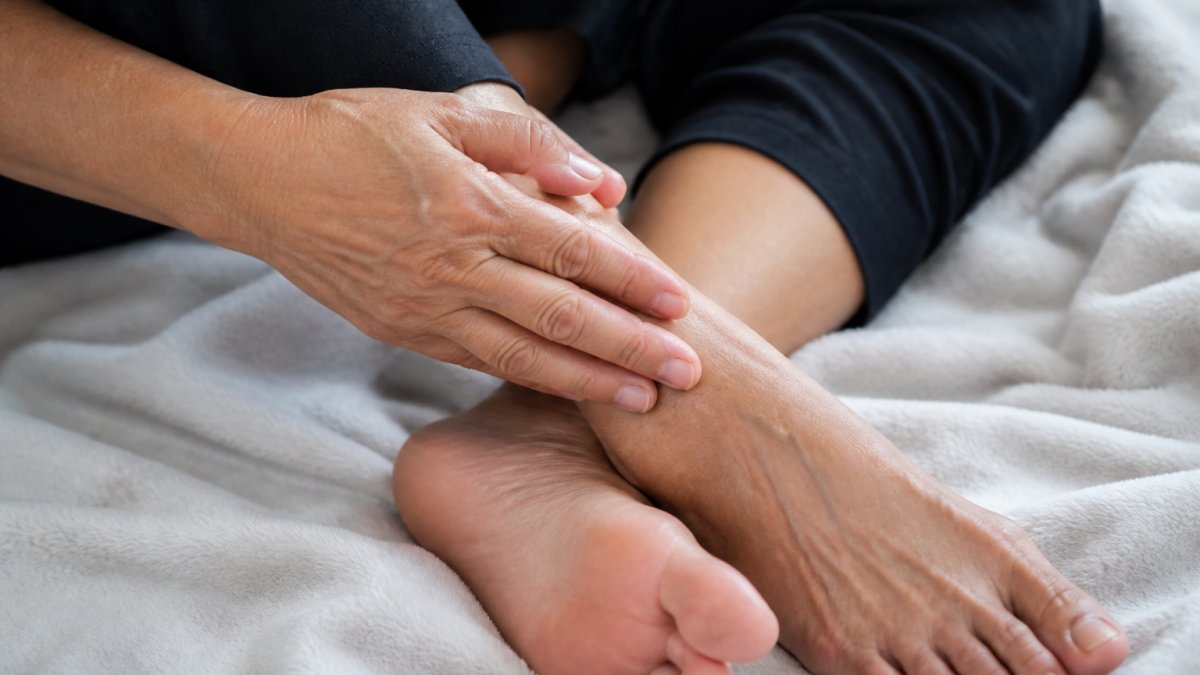Close-up of an adult's hands and feet resting on a soft blanket, with one hand gently touching the other, showing subtle tingling or numbness in the extremities