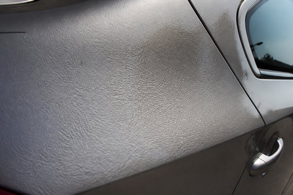 Close-up of vehicle panel showing orange peel texture under natural sunlight, with uneven surface visible across painted area