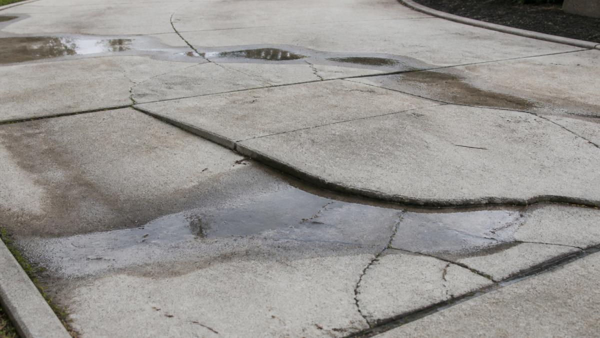 Close-up of concrete driveway surface showing visible cracks, settling, and uneven sections with water pooling in low spots