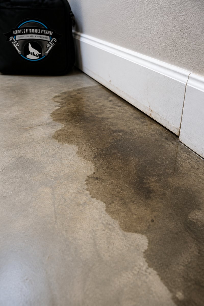 Close-up of damp discoloration on concrete flooring near baseboards showing water damage and moisture infiltration from slab leak