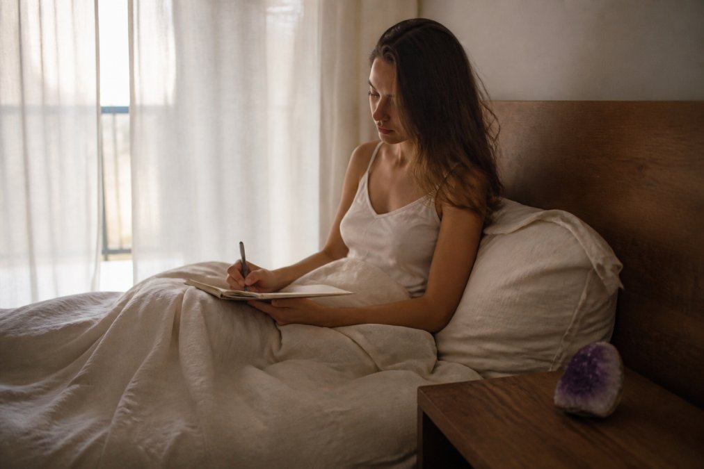 Woman writing in a dream journal at dawn, noticing sleep changes and vivid dreams during spiritual ascension.