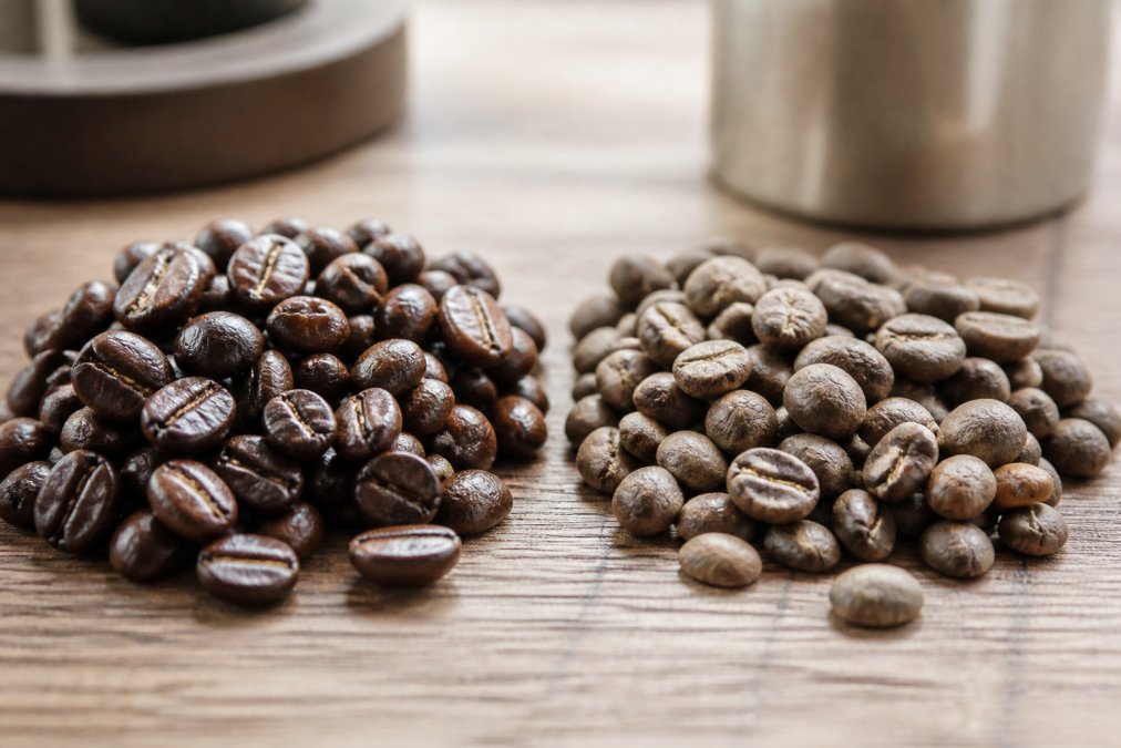 Close-up of fresh vibrant dark brown coffee beans with glossy sheen next to dull, faded, matte-colored stale beans on a wooden surface with natural window lighting