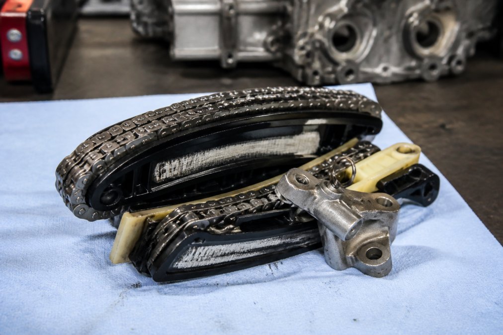 Close-up of a timing chain and tensioner assembly removed from a European engine, resting on a clean shop towel with visible wear marks on the guides