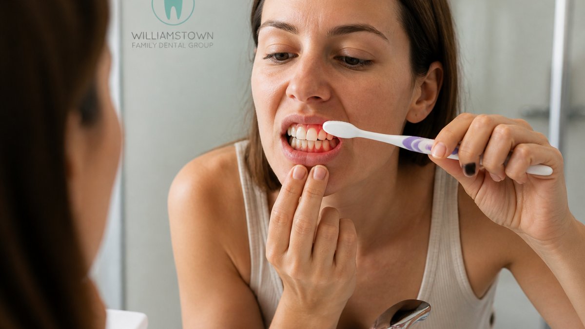 Close-up of a person brushing their teeth at a bathroom sink, showing natural lighting and focus on gum line during dental hygiene routine