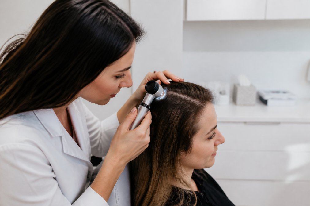 Dermatologist using a dermatoscope to examine a patient’s scalp in a modern clinic room