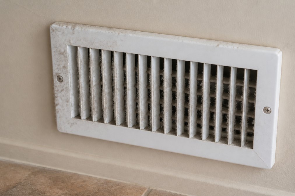 Close-up of a white vent cover showing accumulated dust and debris around the edges and slats in a residential home