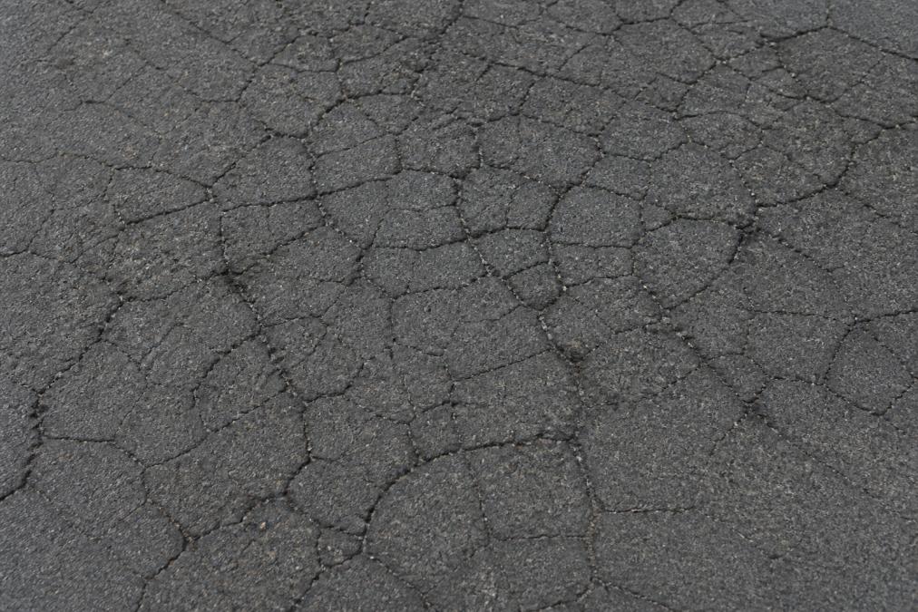 Close-up view of asphalt pavement showing interconnected alligator cracking pattern with multiple fracture lines creating a web-like network across the dark surface
