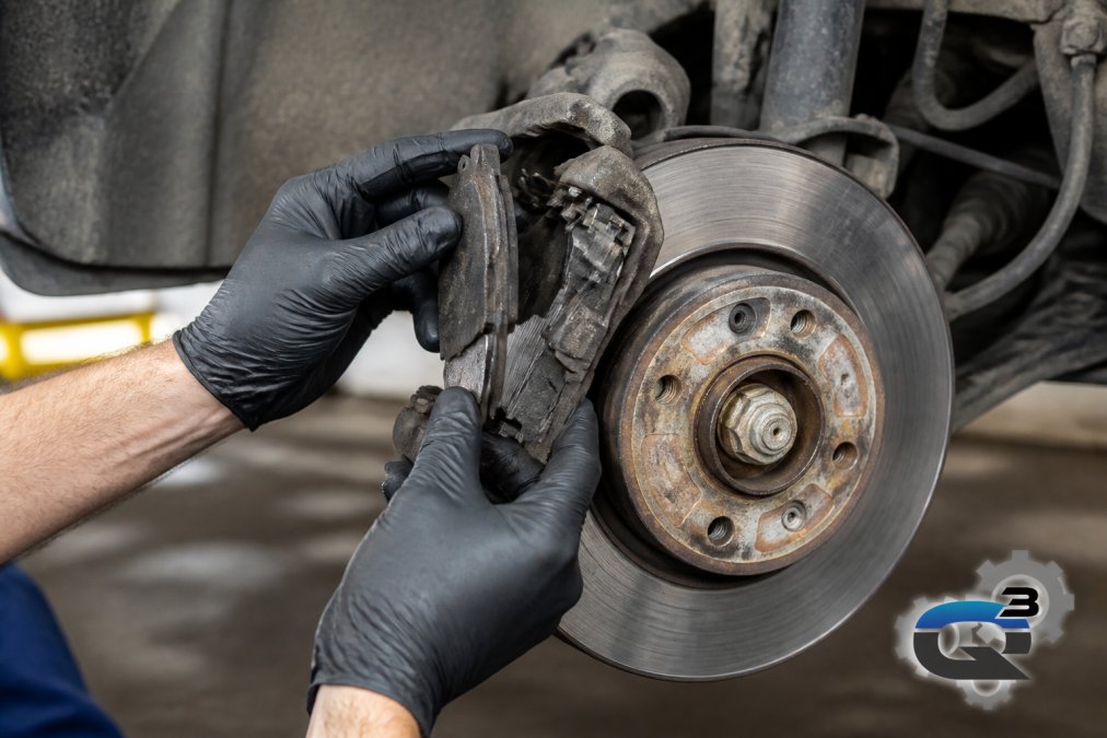 Professional technician's hands inspecting brake pads and rotors on a vehicle wheel, showing worn pad material and rotor surface damage clearly