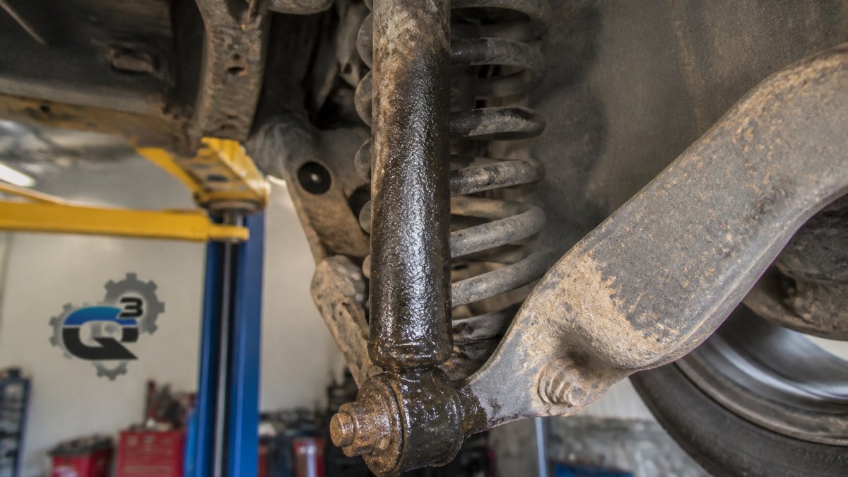 Close-up of a worn shock absorber with visible leaking fluid and corrosion on an older vehicle undercarriage
