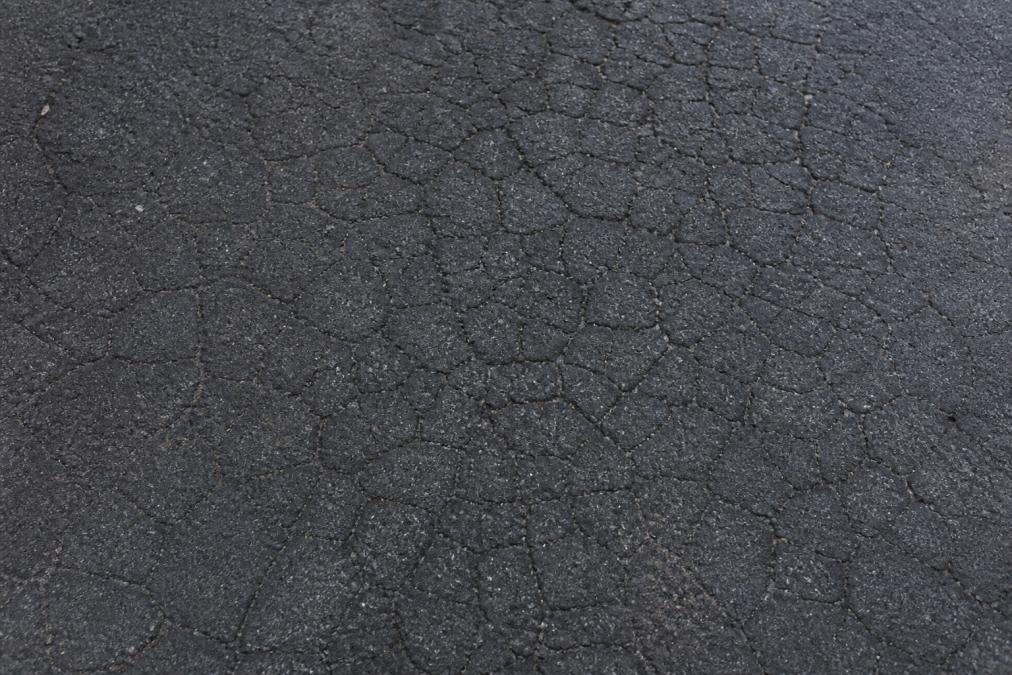 Overhead view of asphalt parking lot surface showing severe alligator cracking pattern with interconnected cracks creating a web-like appearance across the dark pavement