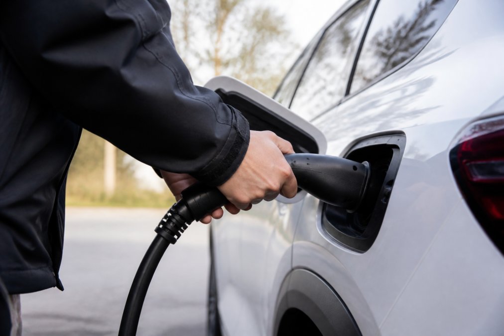 Krupni plan osobe koja spaja V2L adapter na priključak za punjenje tipa 2 električnog automobila po danu, s fokusom na priključak utikača i pravilno umetanje