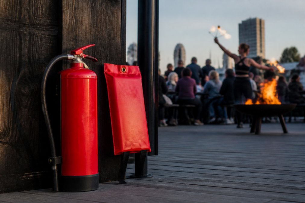 Nærbillede af ildslukker og branddasker opstillet korrekt ved siden af et arrangementsområde med åben ild