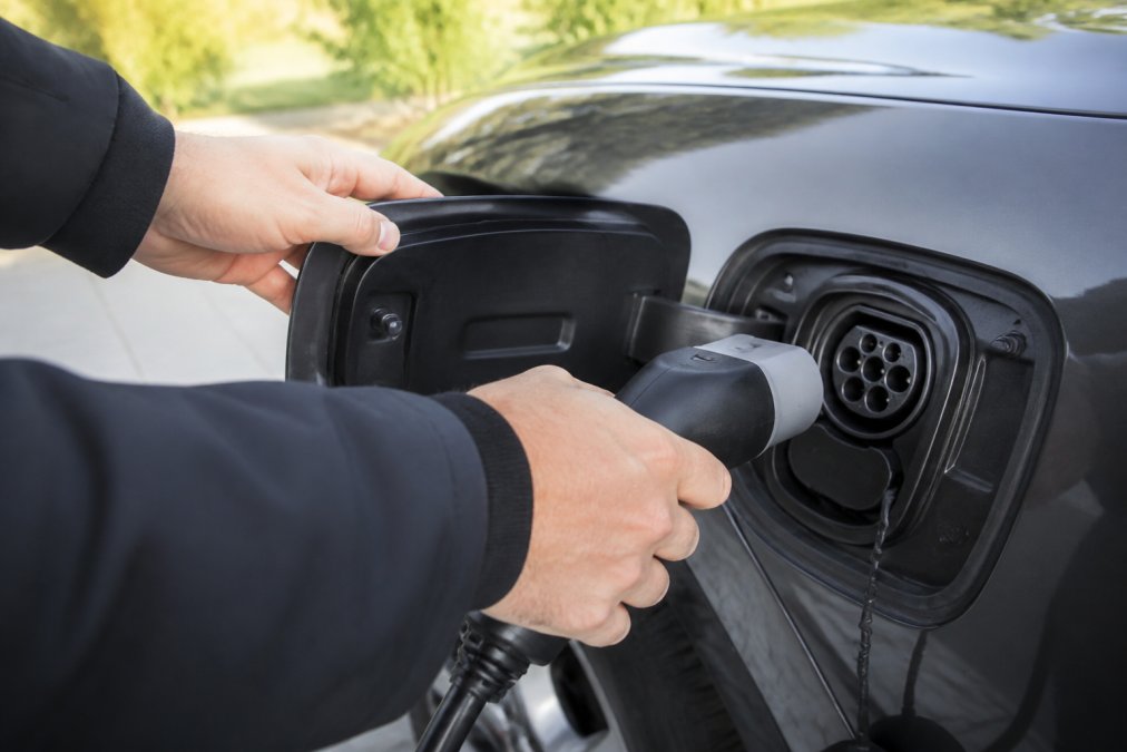 De handen sluiten zorgvuldig Type 2-V2L-kabels aan op de laadpoort van een elektrische auto bij daglicht, waarbij de nadruk ligt op de juiste hantering en een veilige aansluitprocedure.