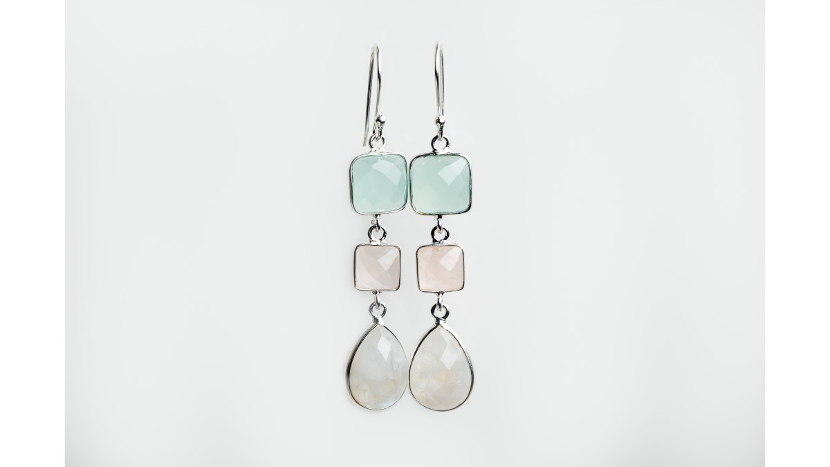 Woman wearing delicate handcrafted jewelry pieces, minimalist sterling silver rings and gemstone drop earrings, displayed in natural daylight with hands gently touching the jewelry