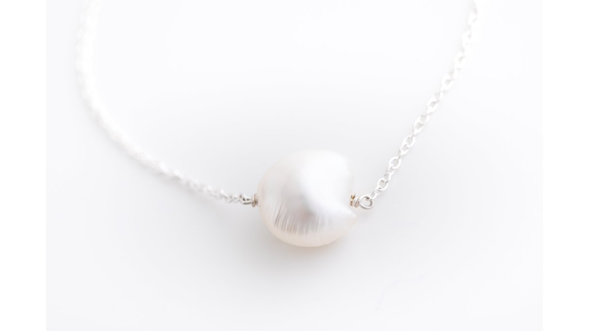 A close-up lifestyle photo of a woman's wrist wearing a delicate sterling silver chain bracelet with a small pearl, resting on neutral linen fabric in soft natural light