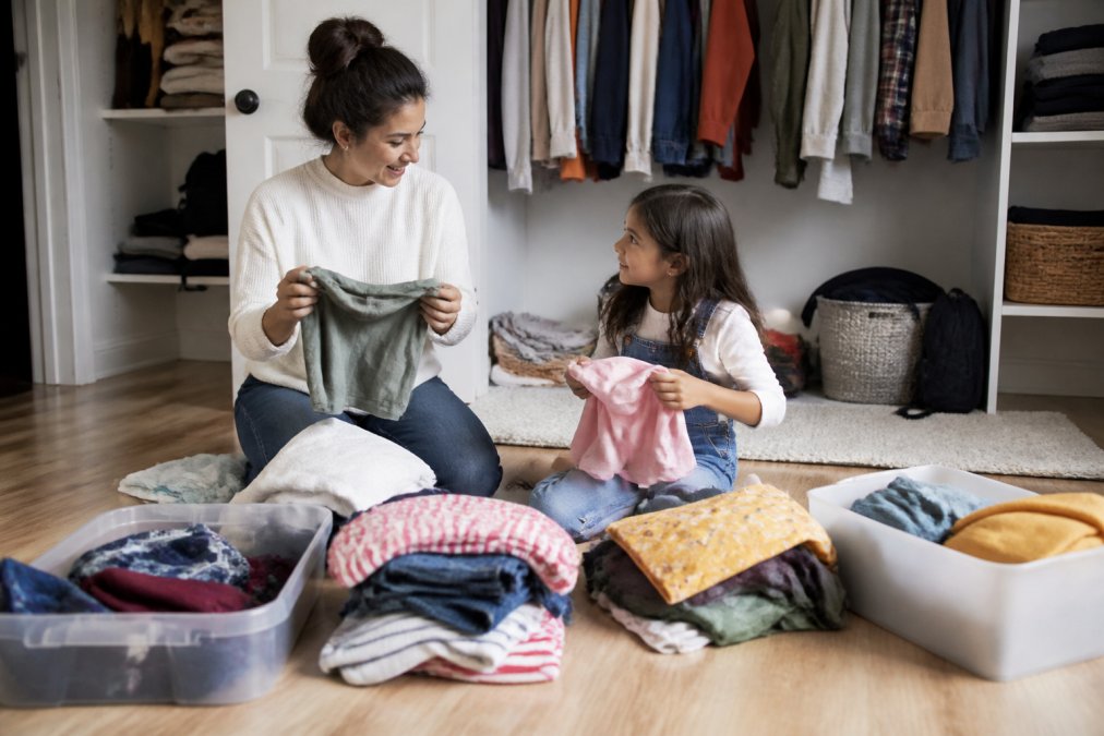 Parent and child sorting through a closet together, with piles of clothing organized on the floor by category, keep, donate, and outgrown items clearly separated