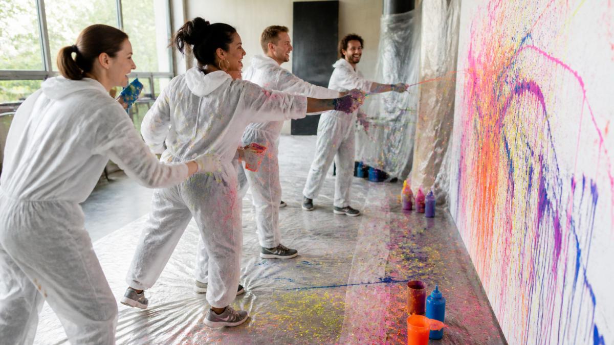 Lachendes Team beim kreativen Malen als Teil abwechslungsreicher Teambuilding Spiele in einem hellen Atelier.
