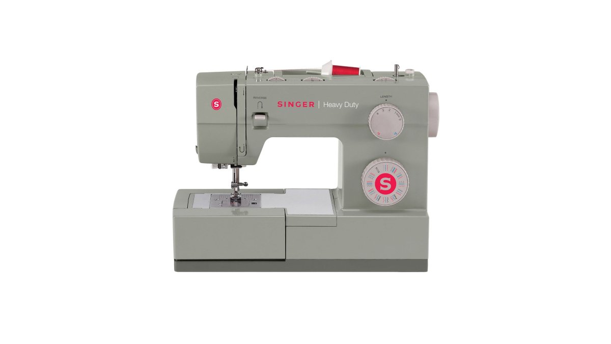 Close-up of hands guiding folded denim under the presser foot of a heavy duty sewing machine, metal frame visible, bright home sewing room