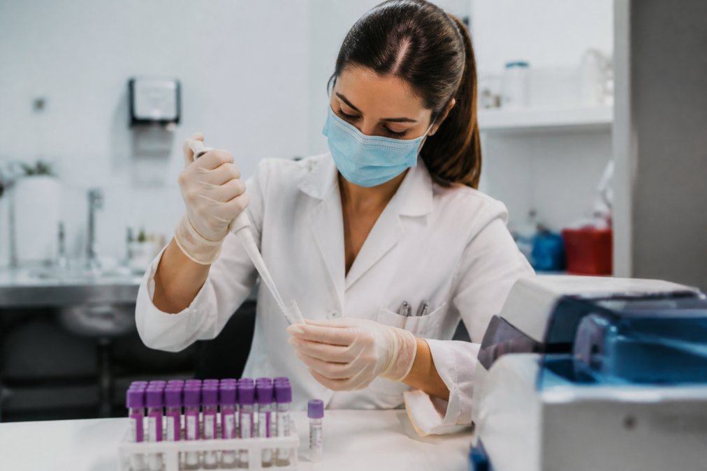 Profesional de laboratorio en clínica moderna preparando muestras para análisis PCR con equipo médico, usando guantes estériles y con tubos de muestras claramente visibles
