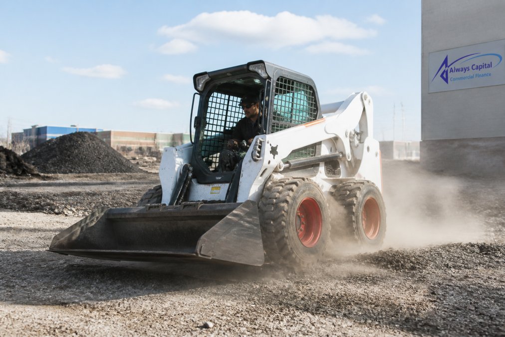 Skidsteer pivoting on a gravel site, featured in our skidsteer guide, kicking up dust while turning in a tight circle.