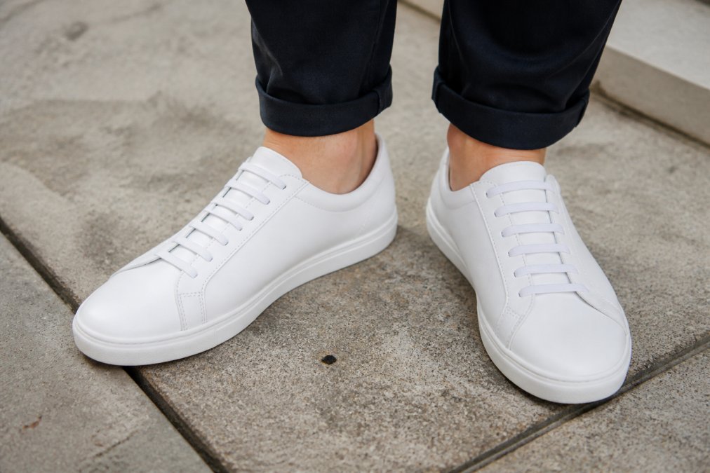 Close-up of a person's feet wearing clean white sneakers with elastic no-tie laces that stay organized and tidy, showing the polished appearance with secure fit and no dangling strings visible, photographed in natural daylight