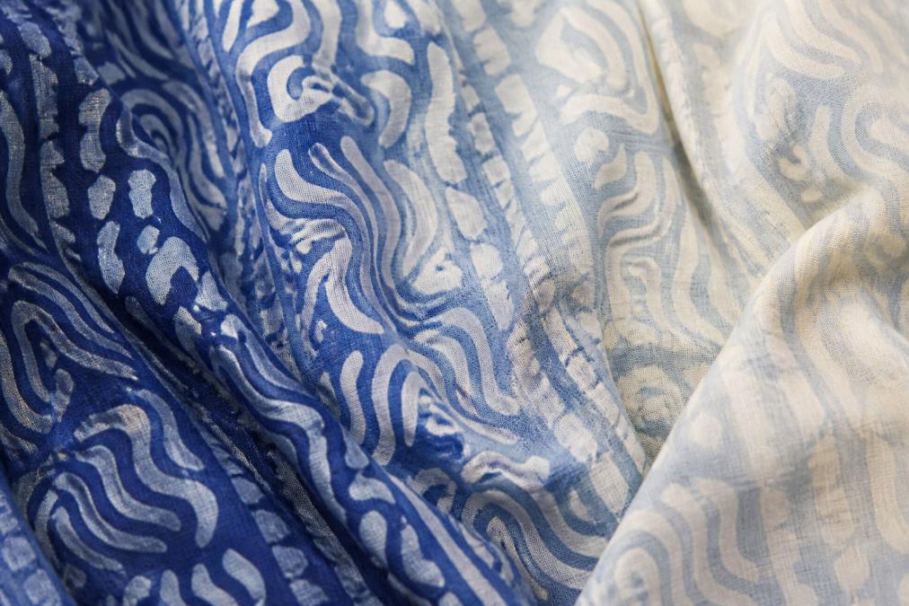 Close-up of finished ombré gradient fabric showing striking color variation from deep indigo blue to pale cream shade, highlighting the unique non-replicable color transitions characteristic of slow-dyed cotton textile with natural light revealing fiber texture