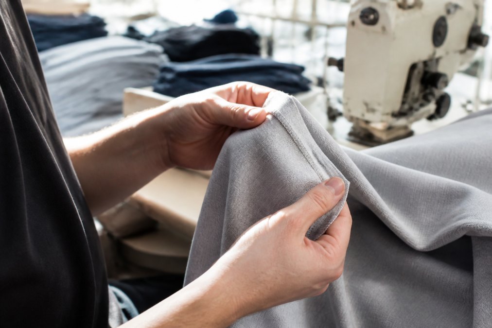 Hands inspecting fabric texture and stitching during small batch clothing production in a sunlit workshop