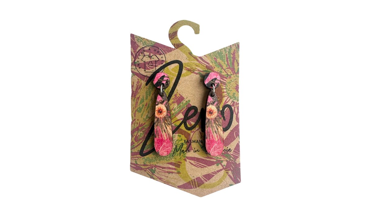 Close-up of handmade Tasmanian oak earrings resting on a wooden workbench with small off-cuts of timber visible in the background, warm natural light from a nearby window