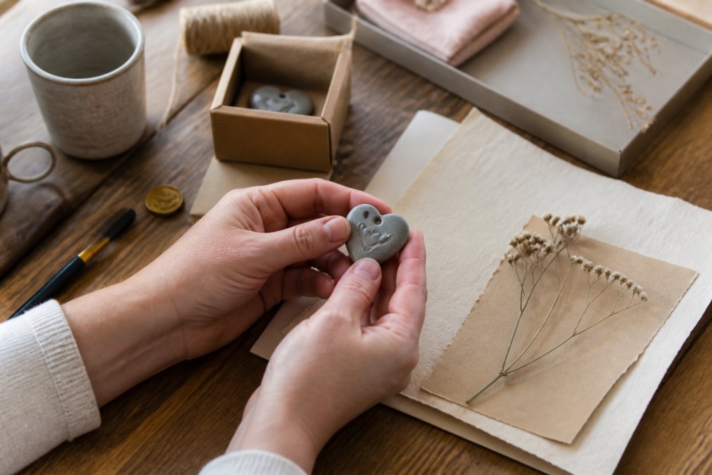 Close-up of hands holding a small hand-finished keepsake token with a handwritten note nearby on soft paper, suggesting a personal gesture of care and support