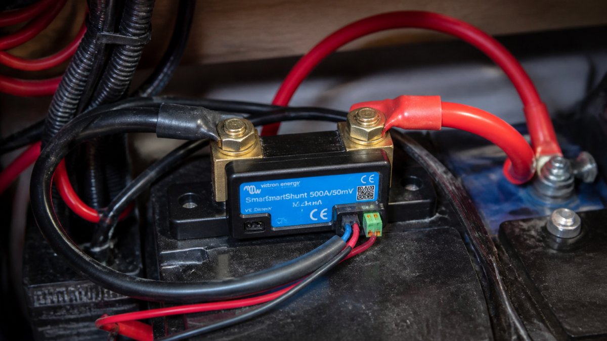 Close-up of a Victron SmartShunt device mounted directly on battery negative terminal with color-coded cable connections clearly visible and labeling readable