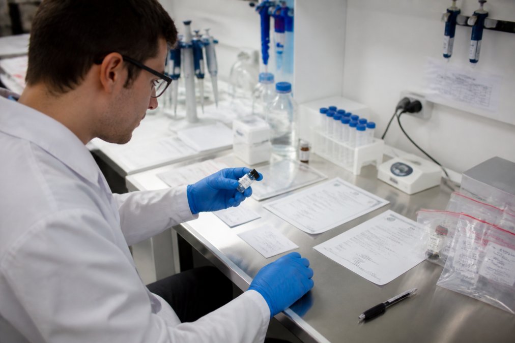 Onderzoeker in laboratoriumomgeving die een peptideproduct onderzoekt met certificaten en documentatie zichtbaar op het werkblad, onder helder laboratoriumlicht