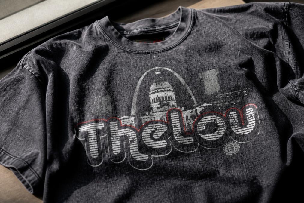 Close-up of a snow washed cotton tee showing the frosty, powdery surface texture with faded color variations and lived-in appearance, with natural window lighting highlighting the fabric's dimensional finish