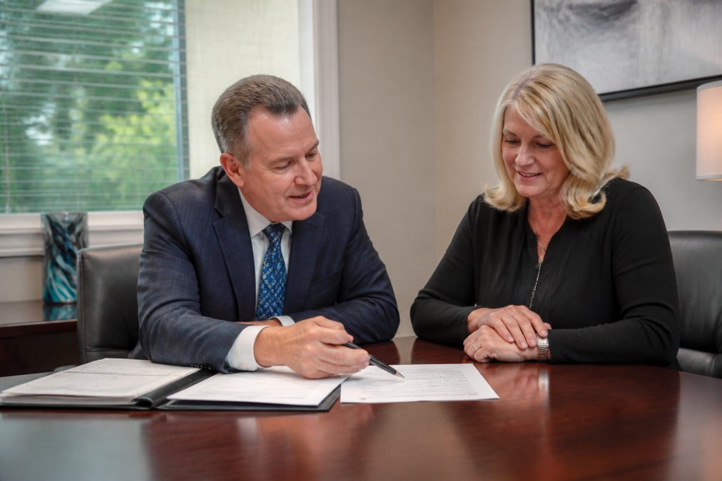 Financial advisor meeting with a client in a professional office setting, pointing to documents on a desk while discussing retirement income strategy in natural daylight