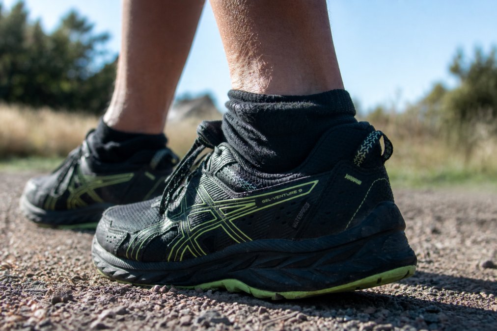 Close-up of a hiker's boot and sock showing proper cuff fit and sock positioning inside the boot during a trail hike, with reinforced heel visible and leg muscle engaged