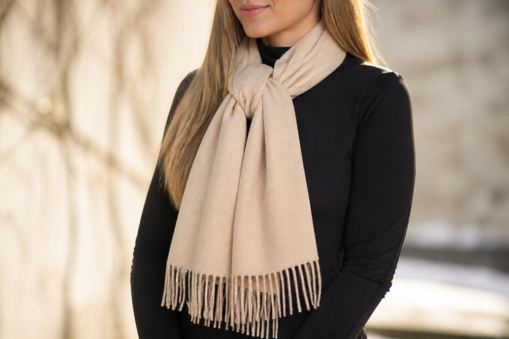 Close-up of a luxuriously soft alpaca scarf draped elegantly over someone's shoulders in winter sunlight, showing the fine brushed texture and natural sheen against neutral winter clothing