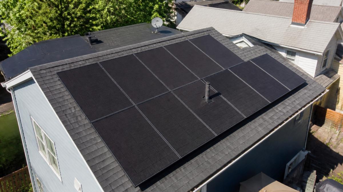Aerial view of residential rooftop with solar panels installed, showing system positioning and integration with home structure, bright daylight