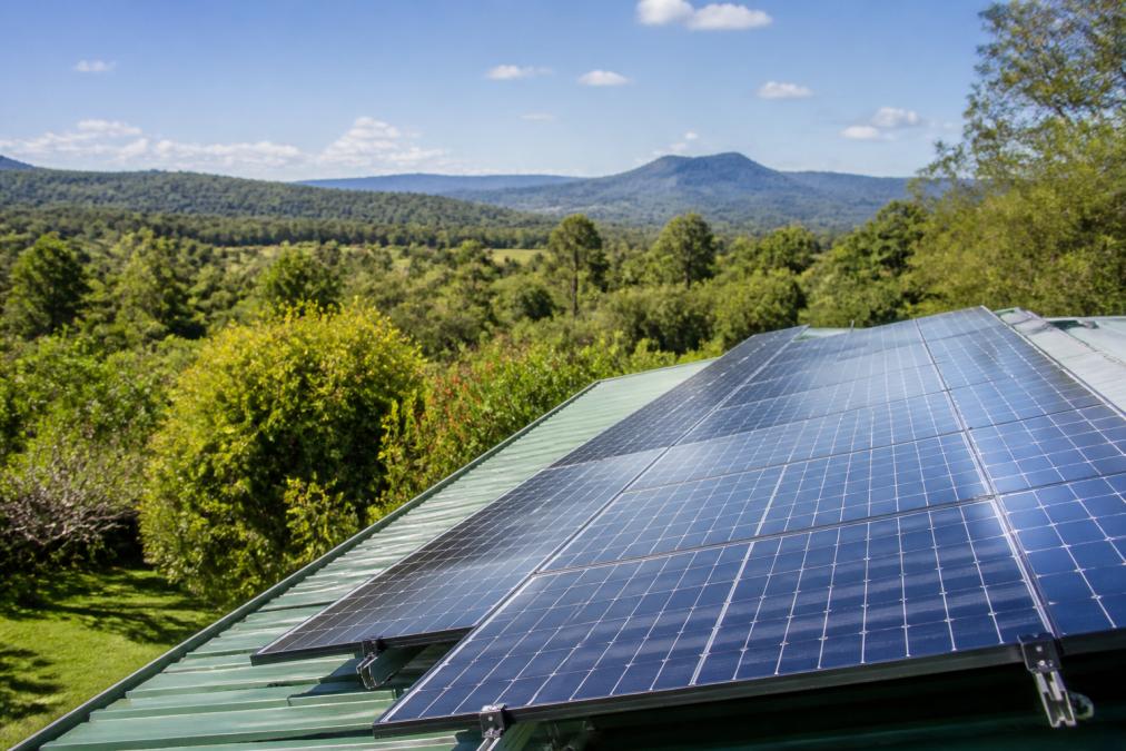 Solar panels mounted on a residential roof with clear sky and green bushland landscape in the background