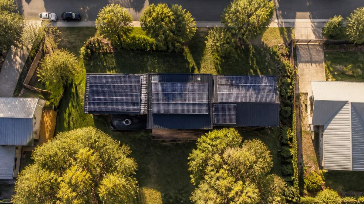 Aerial view of a modular home on a residential block showing roof orientation, surrounding trees, and shadow patterns cast across the structure at different times of day