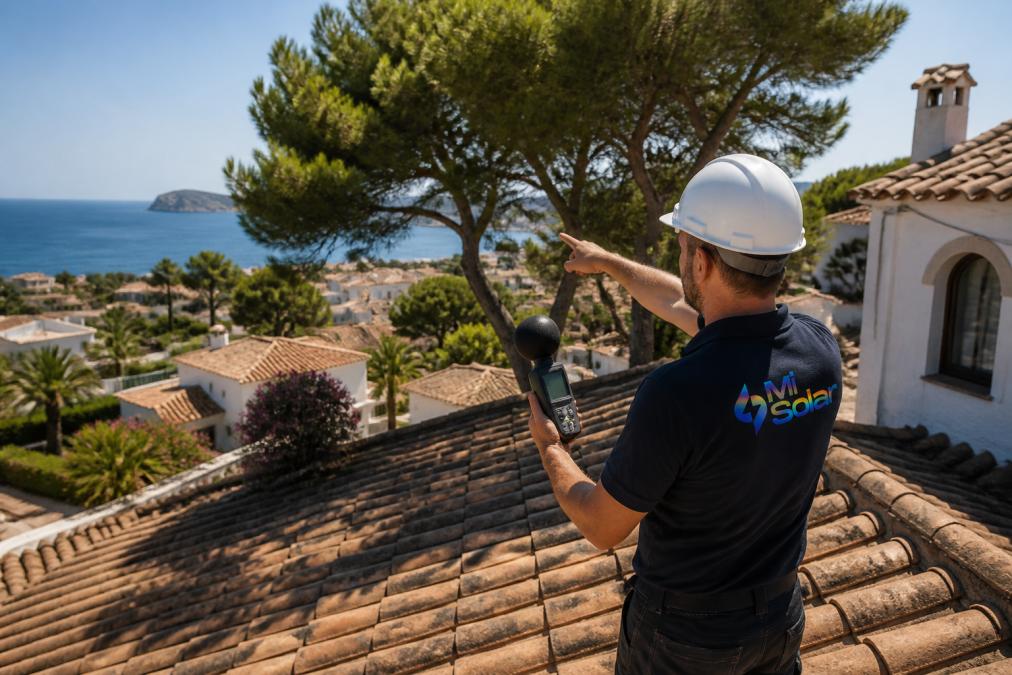 A solar installer standing on a tiled villa roof in a Mediterranean coastal town, holding a shade analysis tool and pointing towards nearby pine trees casting shadows across the roof surface, bright afternoon sunlight