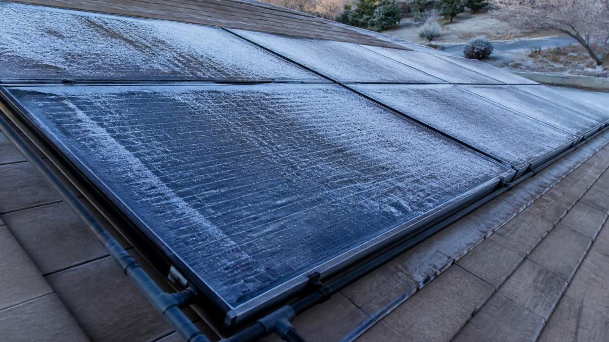 Close-up view of solar pool panels mounted on residential roof with frost accumulating on the collector surface, showing the dark absorber plate and frame typical of Heliocol-style arrays