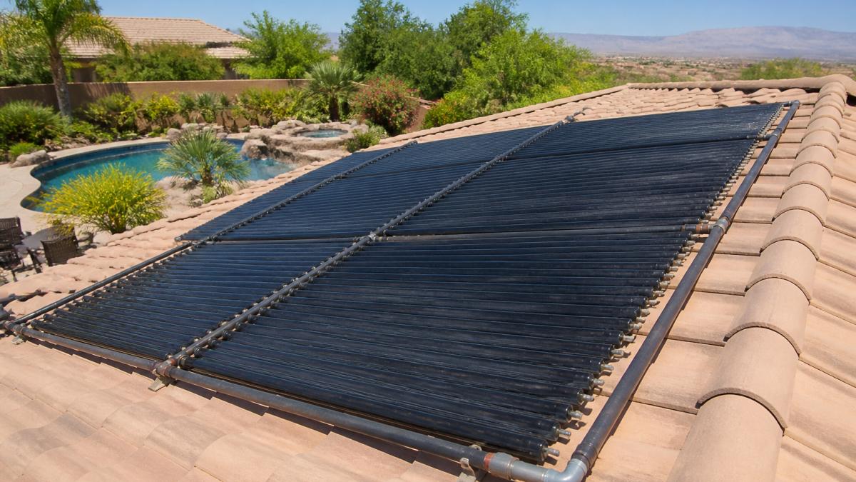 Rooftop solar collector panels installed on residential home with clear blue sky, thermal absorption surface visible, pool area in background