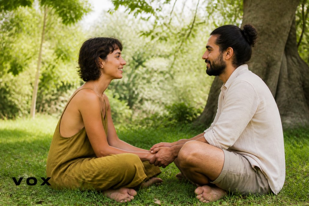 Two people practicing grounding together outdoors, feet on grass, hands gently touching, with trees and natural light in the background