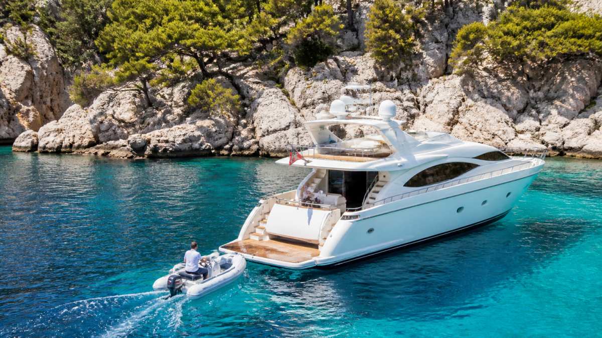 White motor yacht anchored in turquoise water off a rocky Mediterranean cove during a French Riviera yacht charter.