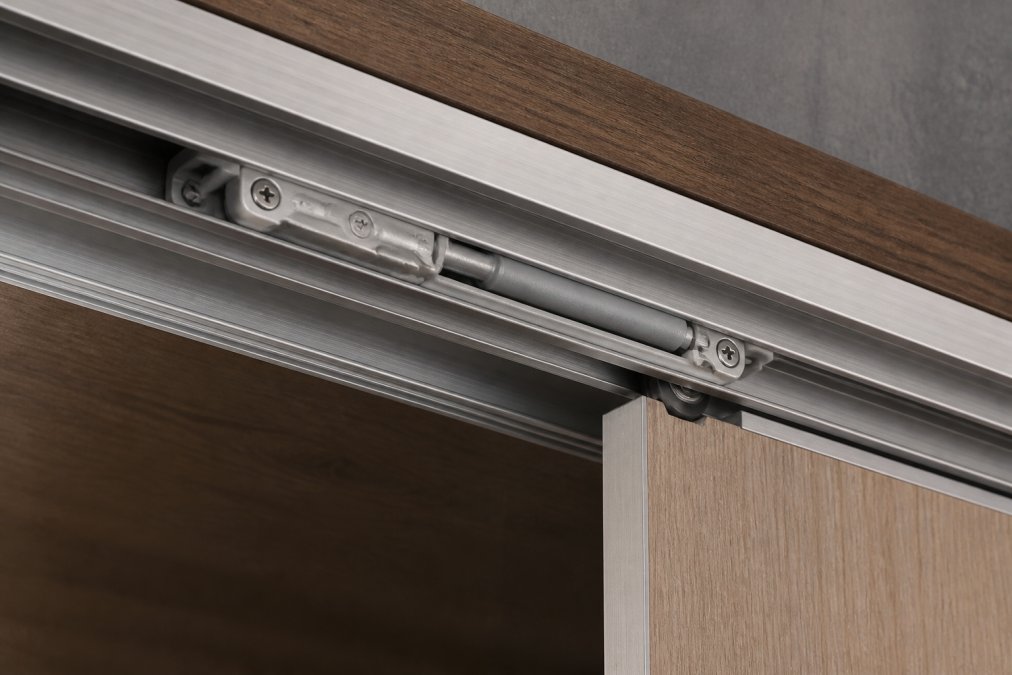 Close-up of precision-engineered aluminium track profile with soft-close damper mechanism, showing the metallic finish and mechanical components of a premium sliding door system installed on a wooden frame