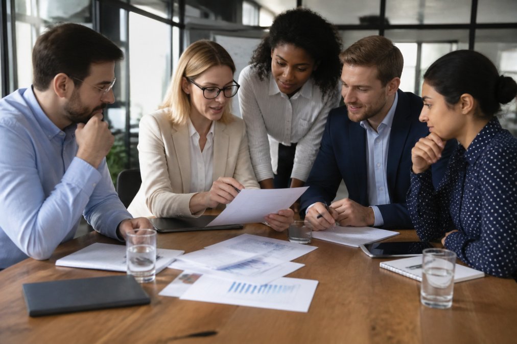 HR professionals and hiring managers collaborating in modern office setting, reviewing talent pipeline charts and candidate progression on screens and documents