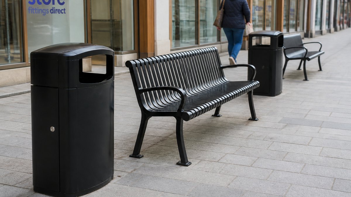 A person walking past a row of outdoor benches and litter bins on a paved pedestrian street outside a shopfront