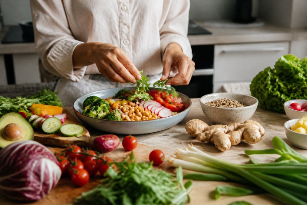 Person preparing a colorful meal with fresh vegetables, whole grains, and ginger root on a clean kitchen counter, demonstrating natural food sources for digestive support and enzyme-rich ingredients