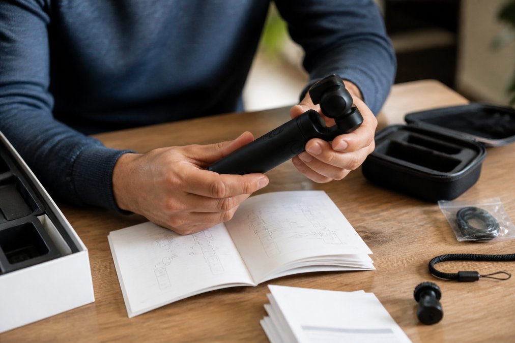 Hands carefully examining a new gadget's build quality and features, with product manual and warranty information visible on workspace, natural studio lighting