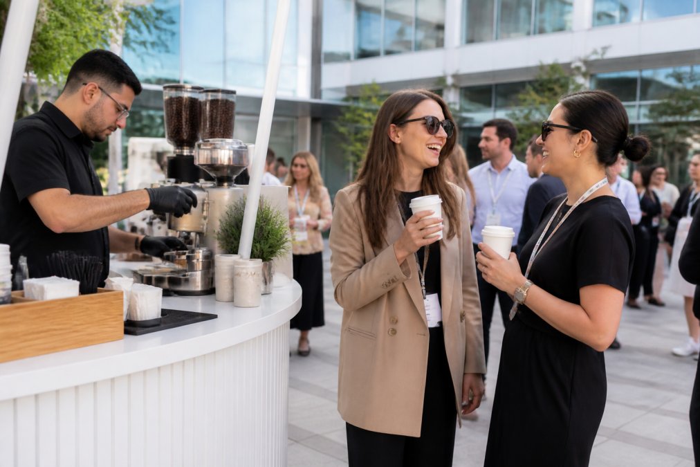 Branded mobile coffee cart at a corporate event with custom cup design and logo, barista preparing specialty drinks, guests holding custom-branded beverages in modern office courtyard