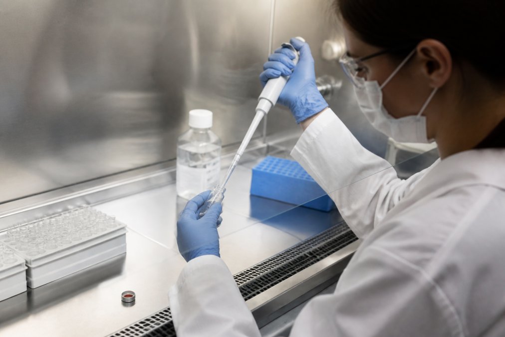 Onderzoeker in laboratoriumjas voorzichtig bacteriostatisch water in een peptideflacon pipetteert met precisie-instrumenten, heldere laboratoriumverlichting, steriele werkbank zichtbaar